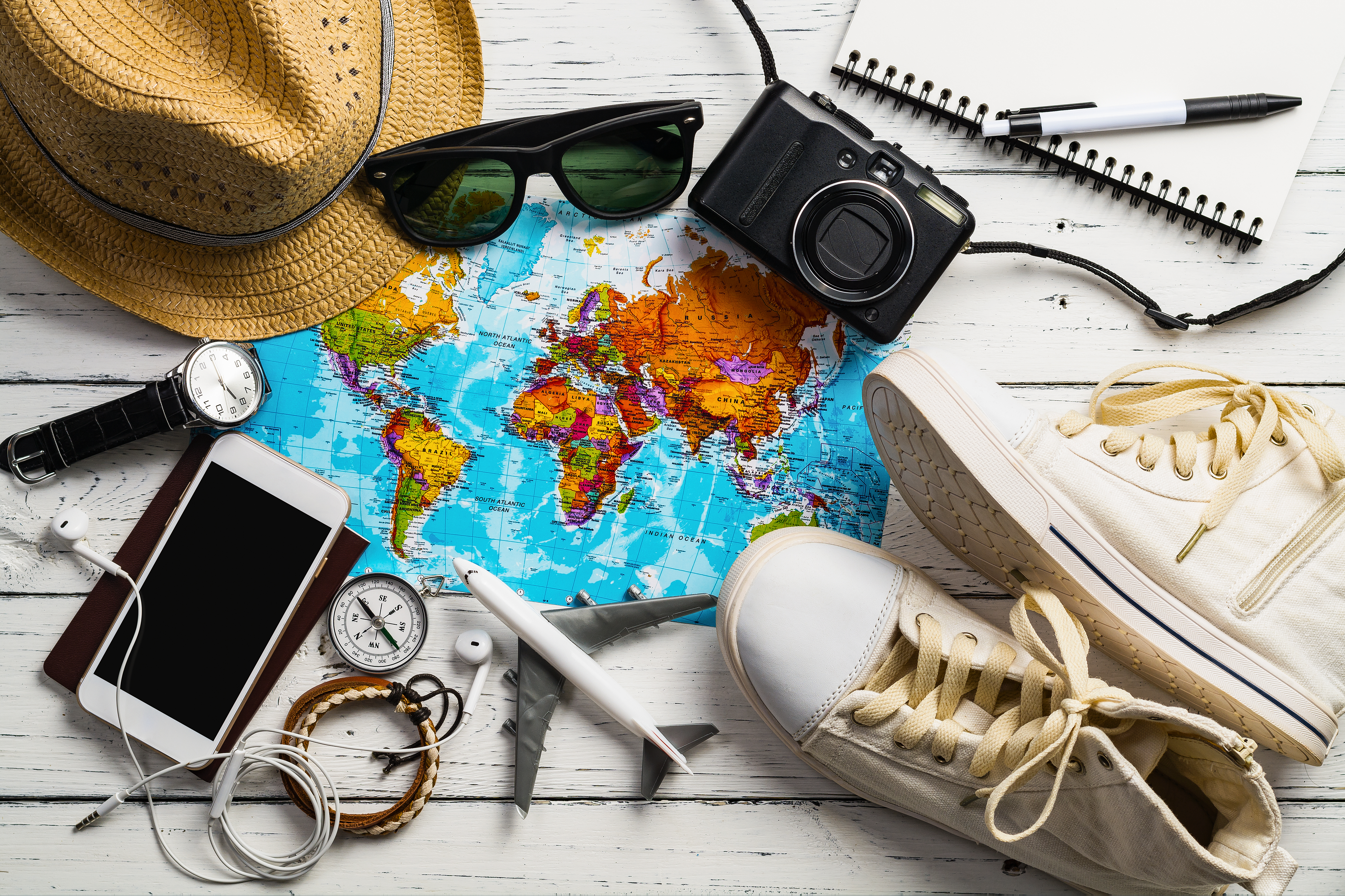 Flatlay of travel essentials, including mobile, hat, shoes and a map