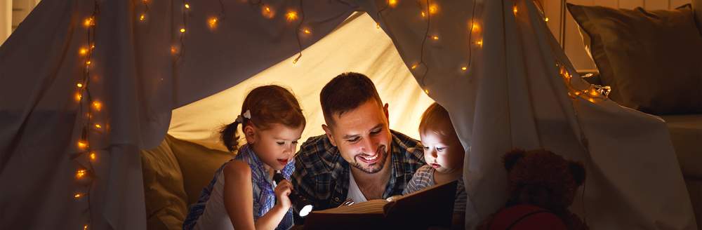 Father and children reading book in homemade den